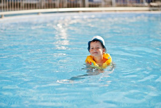 Kleiner Junge mit Schwimmflügeln im Wasser